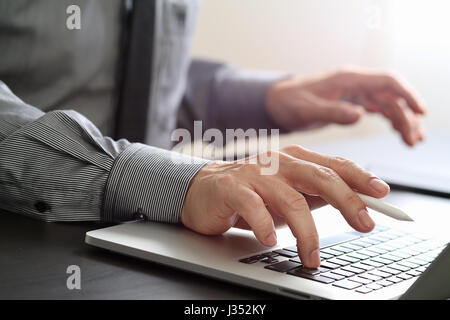 close up of businessman working with mobile phone and stylus pen and laptop computer  on wooden desk in modern office Stock Photo