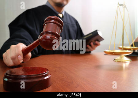 justice and law concept.Male judge in a courtroom with the gavel and working with smart phone and brass scale on wood table Stock Photo