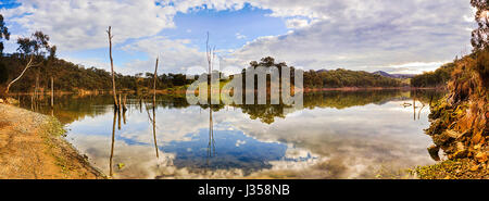 Panorama of quiet still waters in Lake Lyell on Coxs river. Sunny warm day with clouds reflect in blue surface between rocky shores and gumtree woods. Stock Photo
