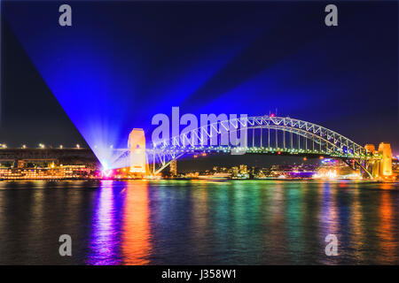 Projection from The Rocks under the Sydney Harbout bridge during Vivid Sydney light show festival. Illuminated arch of bridge reflects in blurred harb Stock Photo
