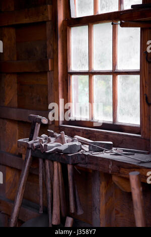 Tools in an old blacksmith forge. A number of hammers of different sizes with wooden handles inserted in a wooden platform installed by the window. Stock Photo