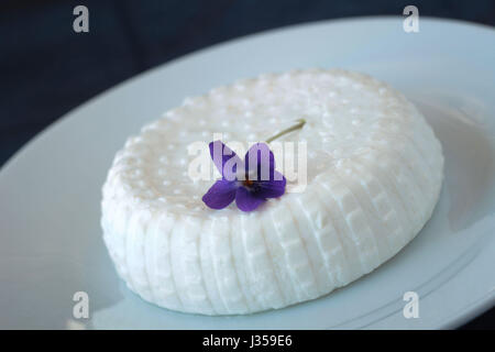 Fresh soft goat cheese on white plate with spring flower decoration; close up view Stock Photo