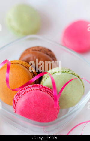 Raspberry, chocolate, pistachio and coffee macaroons in a bowl on white background; close up view Stock Photo