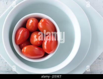 Fresh little plum tomatoes in white bowls on white rustic background; top view Stock Photo