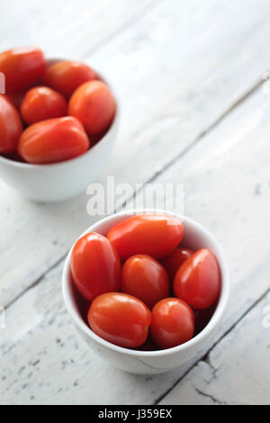 Fresh little plum tomatoes in two white bowls on rustic white background; selective focus Stock Photo