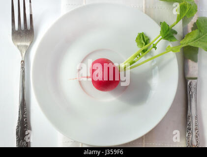 One red radish on white plate with light background with fork and knife; close up high angle view Stock Photo
