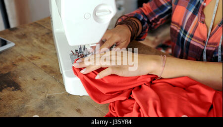 Crop faceless shot of female tailor using sewing machine and making dress with vibrant fabric. Stock Photo