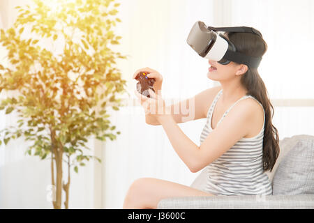 Young happy woman playing video games virtual reality glasses in apartment. cheerful people having fun with new trends technology. mixed race asian ch Stock Photo