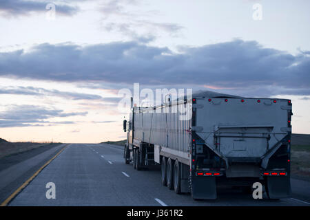 The long professional model in the American big rig semi truck with a two bulk trailers moving with cargo on the evening highway road in Arizona Stock Photo