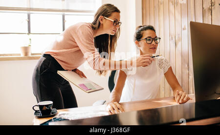 Creative business women working on desktop computer together in office. Two female coworkers working and looking at computer monitor. Stock Photo