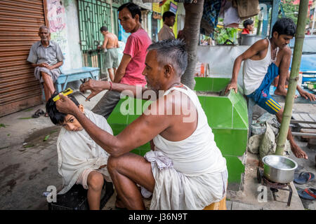 A man cuts hair to a child in the streets of Kumartuli, Kolkata's potters colony Stock Photo