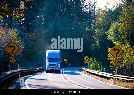 Large American professional powerful truck with smoke from the exhaust pipe, transports goods on the winding road through the mountains Stock Photo