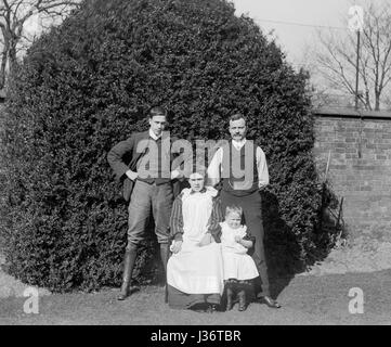 An Edwardian family, two men, a lady and a child, pose for a full length  portrait in front of a large tree in a garden. Photograph taken in 1910 Stock Photo