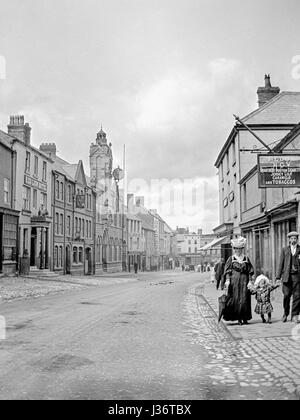 Looking down a wide street in Victorian England, a couple with a small child waking on the right hand side.Image taken circa 1900 Stock Photo