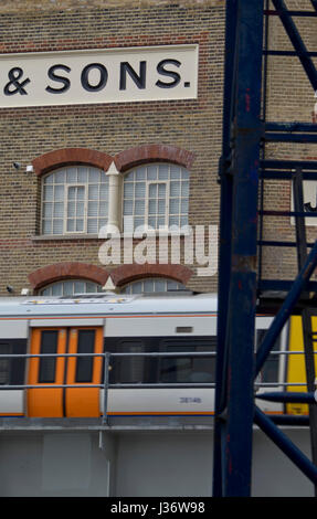 Overground train drives past refurbished old commercial sign on a wall in Hoxton,London,UK Stock Photo