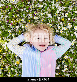 Child on green grass lawn with daisy and dandelion flowers on sunny summer day. Kid playing in garden. Little boy dreaming and relaxing. Kids on Easte Stock Photo