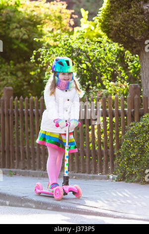 Child riding scooter on way back to school. Little girl playing outdoors learning to balance on kick board. Kids ride scooters in suburbs street. Pres Stock Photo