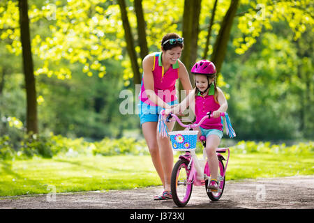 Child riding bike. Kid on bicycle in sunny park. Mother teaching little girl to cycle. Preschooler learning to balance wearing safe helmet. Sport for  Stock Photo