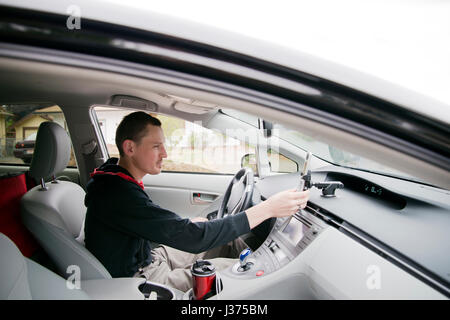 Young driver with a smile and good mood adjusts hand touch screen navigation on mobile phone while sitting behind the wheel of a modern luxury car to  Stock Photo