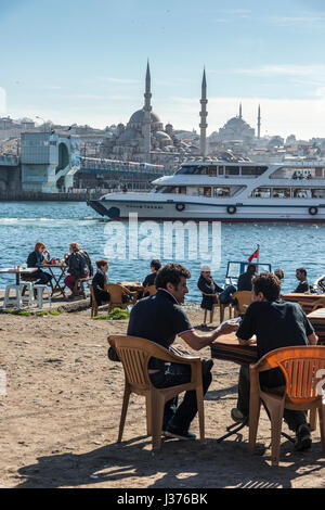 Cafe on Karakoy waterfront, looking across the Golden Horn toward the Yeni mosque at Eminonu  and the Istanbul skyline. Istanbul, Turkey. Stock Photo