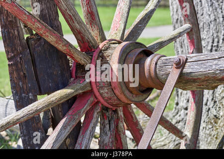 conestoga wagon wheel resting against split-rail fence in barnyard Stock Photo