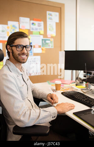 Portrait of smiling designer sitting at desk in creative office Stock Photo