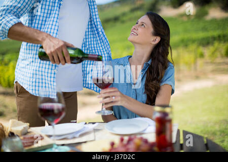 Smiling woman looking at man pouring red wine in glass at table Stock Photo