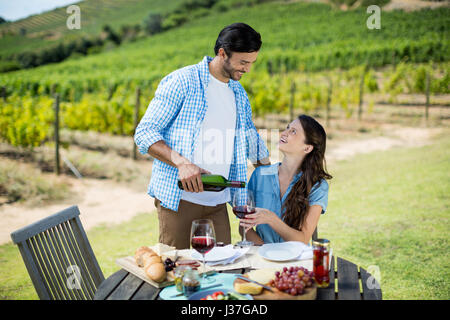 Happy looking at woman while pouring red wine in glass with vineyard in background Stock Photo