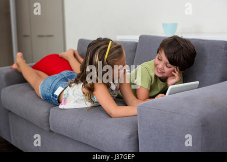 Siblings interacting with each other while using digital tablet in living room Stock Photo