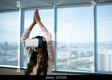 Businesswoman practicing yoga with arms raised while using virtual reality glasses at office Stock Photo