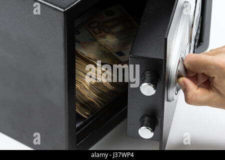 Man's hand opening the door of a safe deposit box full of money Stock Photo