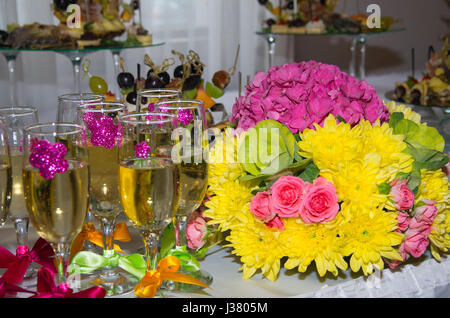 Festive table. Glasses of champagne decorated with ribbons. Bunch of flowers. Fruit snacks Stock Photo