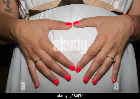 Pregnant woman shows her feelings for the expected baby with hands placed on the abdomen in the form of heart. Stock Photo