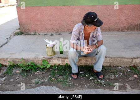 Street scene in Trinidad, Sancti Spiritus, Cuba. Local cuban man sitting on sidewalk with beer and a can. Poverty and loneliness concept. Stock Photo