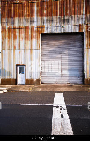 The front side of a large retro old warehouse from sheet of corrugated metal with a closed gate, rusted by time and rain, with front road markings Stock Photo
