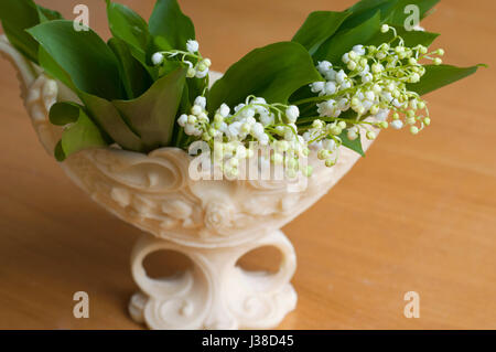 Beautiful bouquet of lily of valleys in an elegant vase isolated on the wooden background Stock Photo