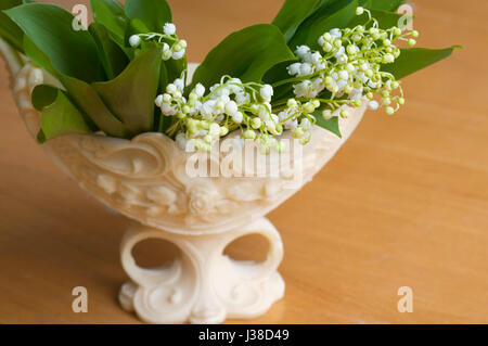 Beautiful bouquet of lily of valleys in an elegant vase isolated on the wooden background Stock Photo