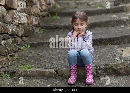 Little girl sitting on the stairs on rainy day Stock Photo