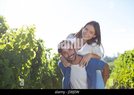 Portrait of happy young couple piggybacking at vineyard during sunny day Stock Photo