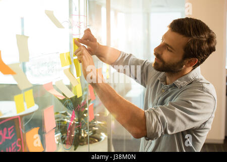 Young businessman sticking adhesive notes on glass at office Stock Photo