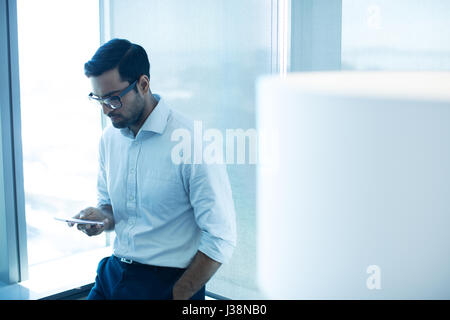 Young businessman using mobile phone while leaning on glass window at office Stock Photo