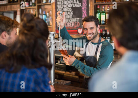 Smiling bartender pouring beer in glass for customers at bar Stock Photo