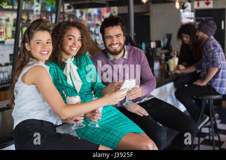 Portrait of cheerful friends discussing over mobile while having drink in restaurant