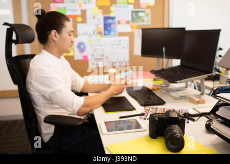 Side view of designer using phone at creative office desk Stock Photo