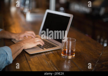 Cropped hands of man using laptop by beer glass at pub Stock Photo