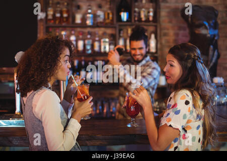 Two young women having cocktail drinks at counter in pub Stock Photo