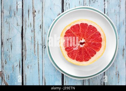 Fresh pink grapefruit half on plate with rustic blue wood background Stock Photo