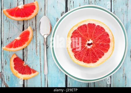 Fresh pink grapefruit slices on plate with rustic blue wooden background Stock Photo