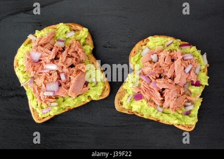 Open avocado sandwiches with tuna, red onion and chia seeds on whole grain bread against a dark slate background Stock Photo