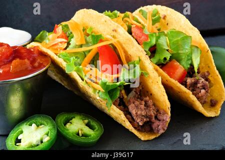 Hard shelled tacos with ground beef, lettuce, tomatoes and cheese close up, on slate background Stock Photo